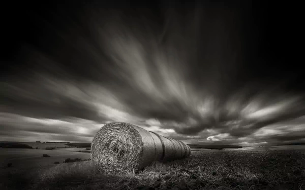 Black and white HD desktop wallpaper of a dramatic cloudscape over a rural field with a large haystack in the foreground, showcasing nature’s serene yet powerful landscape.