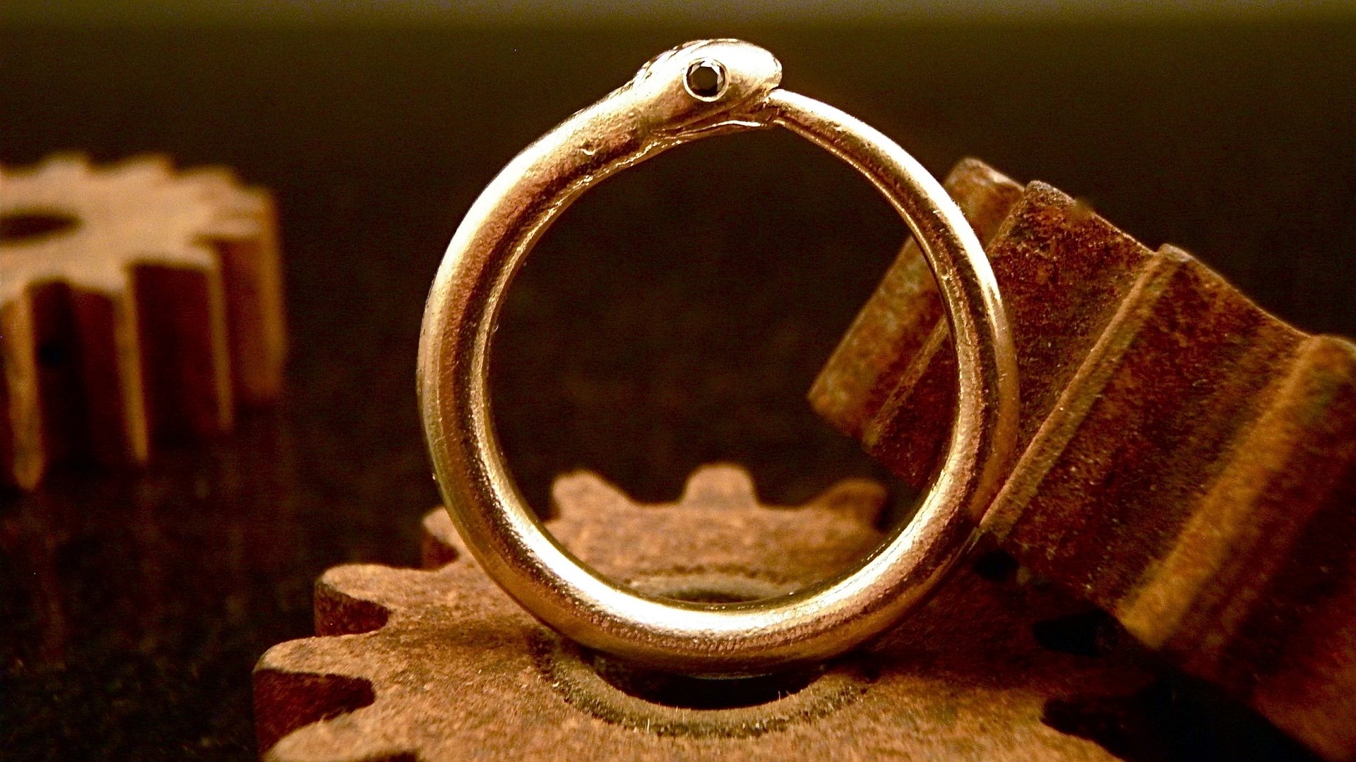 HD fantasy desktop wallpaper featuring a detailed ouroboros ring resting on rusty mechanical gears, symbolizing eternity and cyclical time.