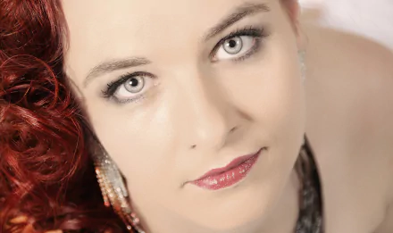 Close-up of a redhead woman with blue eyes, wearing earrings and lipstick, posing as a model for an HD PC desktop wallpaper background.