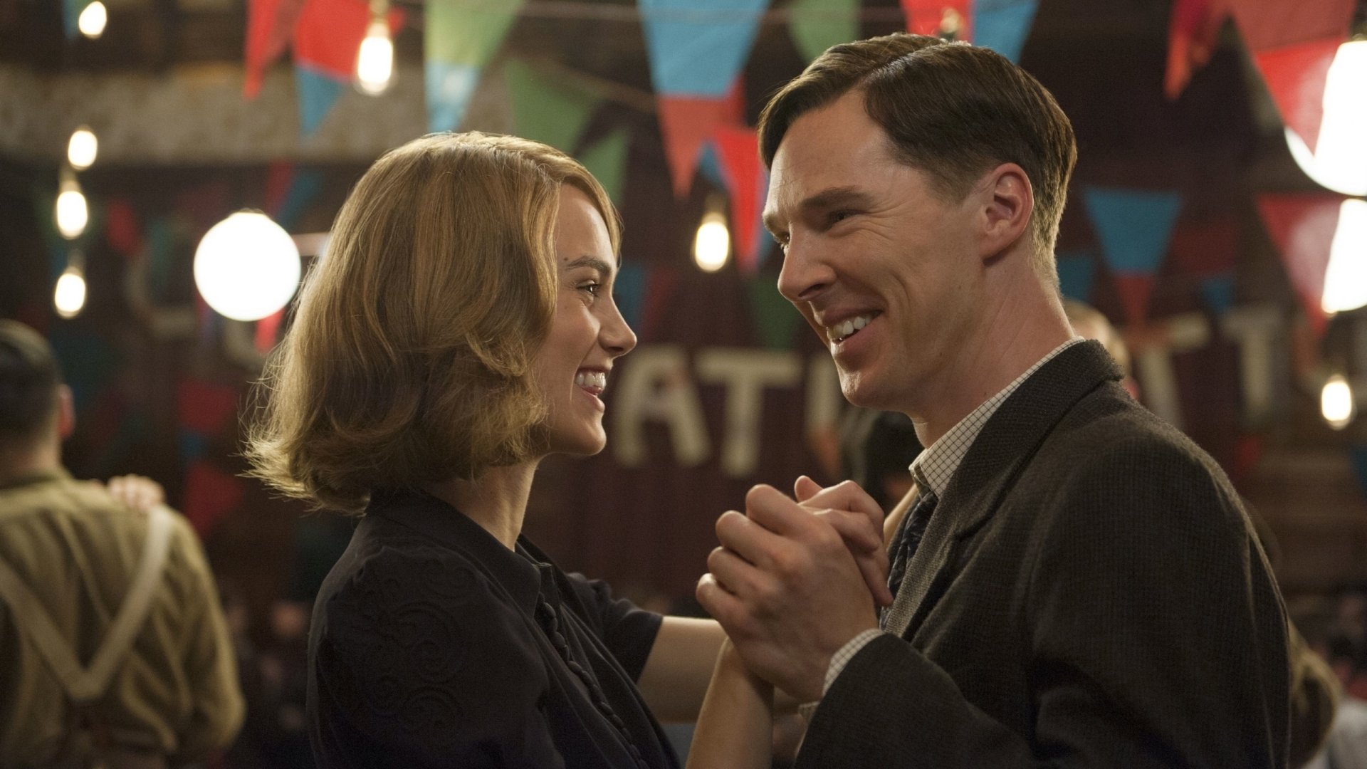 Keira Knightley and Benedict Cumberbatch share a joyful dance scene from the movie The Imitation Game, set against a backdrop of colorful decorations and soft lighting.