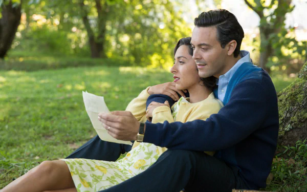 HD PC desktop wallpaper featuring a romantic scene from the movie The Longest Ride, showing a couple sitting on grass, reading a letter together in a sunlit park.