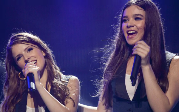 HD desktop wallpaper featuring two female singers performing a scene from the movie Pitch Perfect 2, set against a vibrant stage background.