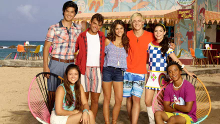 HD PC desktop wallpaper featuring the cast of the movie Teen Beach 2 standing on a beach with colorful rides and decorations in the background.