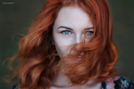 A close-up of a redheaded woman with striking green eyes, her hair flowing softly around her face, set against a beautifully blurred background. An engaging HD desktop wallpaper.