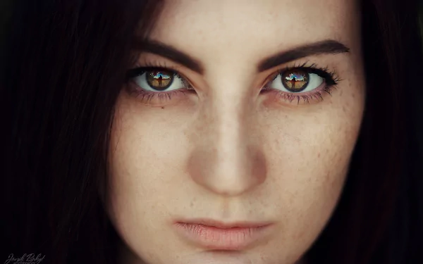 Close-up HD portrait of a woman with brown eyes and freckles, captured with a reflective light enhancing the detailed texture of her face.