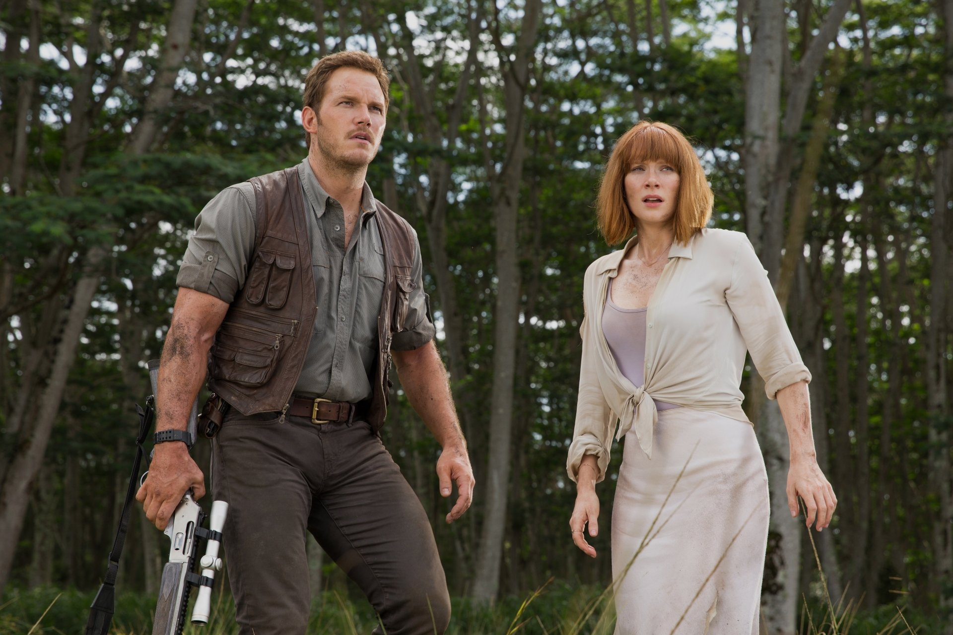 Bryce Dallas Howard and Chris Pratt stand together in a forest setting, showcasing a scene from the movie Jurassic World. This vibrant 4K Ultra HD wallpaper enhances any desktop.
