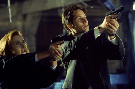 The X-Files TV show 2K Quad HD PC desktop wallpaper: two suited agents aim handguns in a dim, industrial setting, creating a tense, dramatic investigative mood.