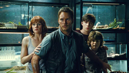 A dramatic scene from Jurassic World featuring Bryce Dallas Howard, Chris Pratt, Nick Robinson, and Ty Simpkins, set against a backdrop of dinosaur exhibits.