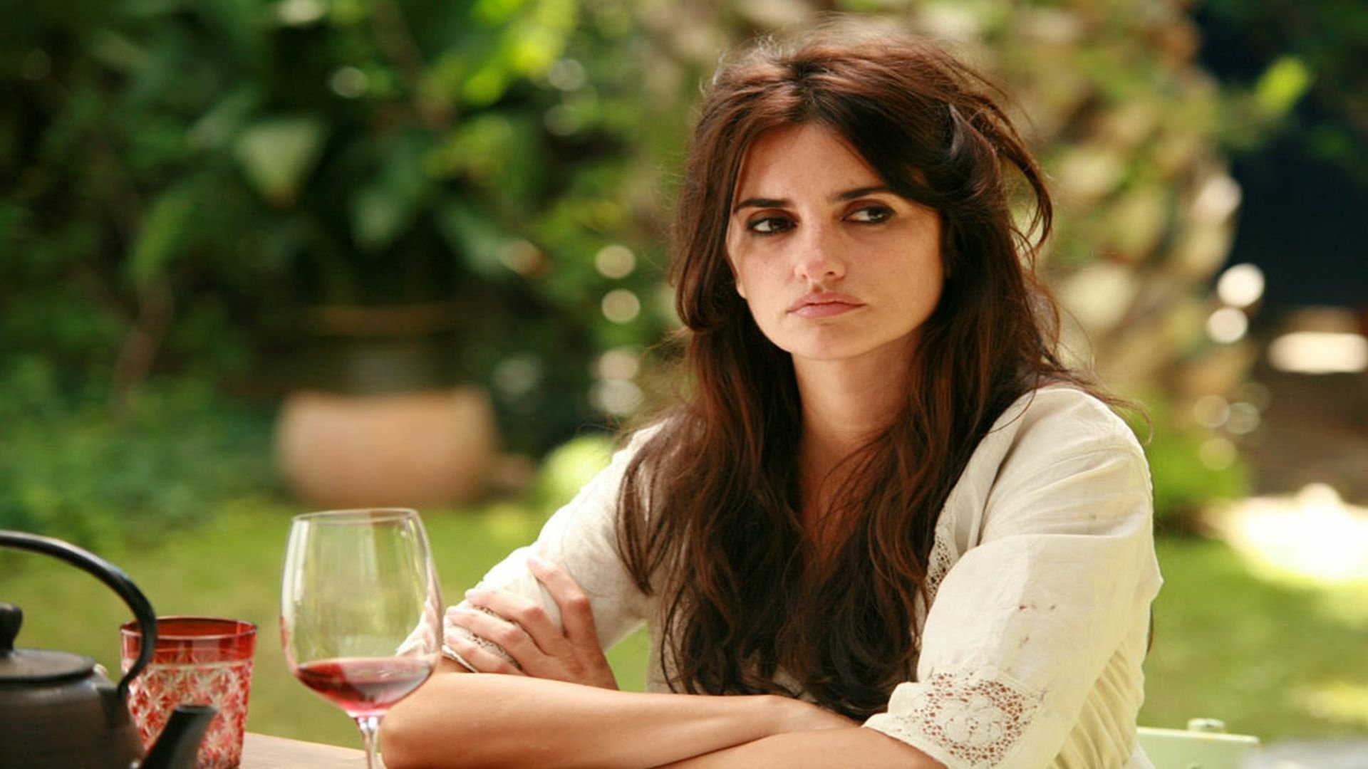 HD PC wallpaper: pensive woman at an outdoor café table with a glass of red wine, cinematic still evoking the movie Vicky Cristina Barcelona.