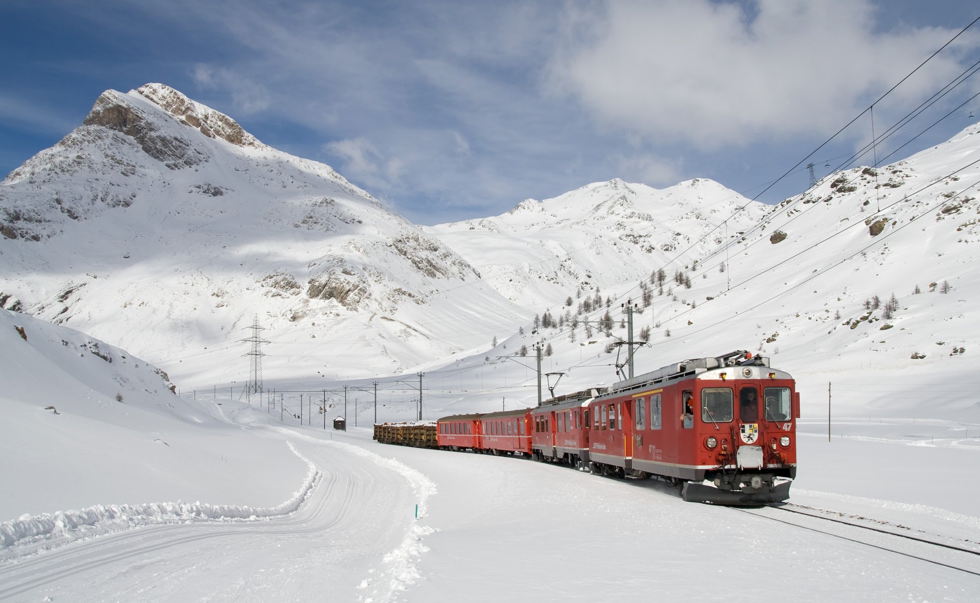 HD desktop wallpaper showing a red train traveling through a snowy mountainous landscape under a partly cloudy sky.