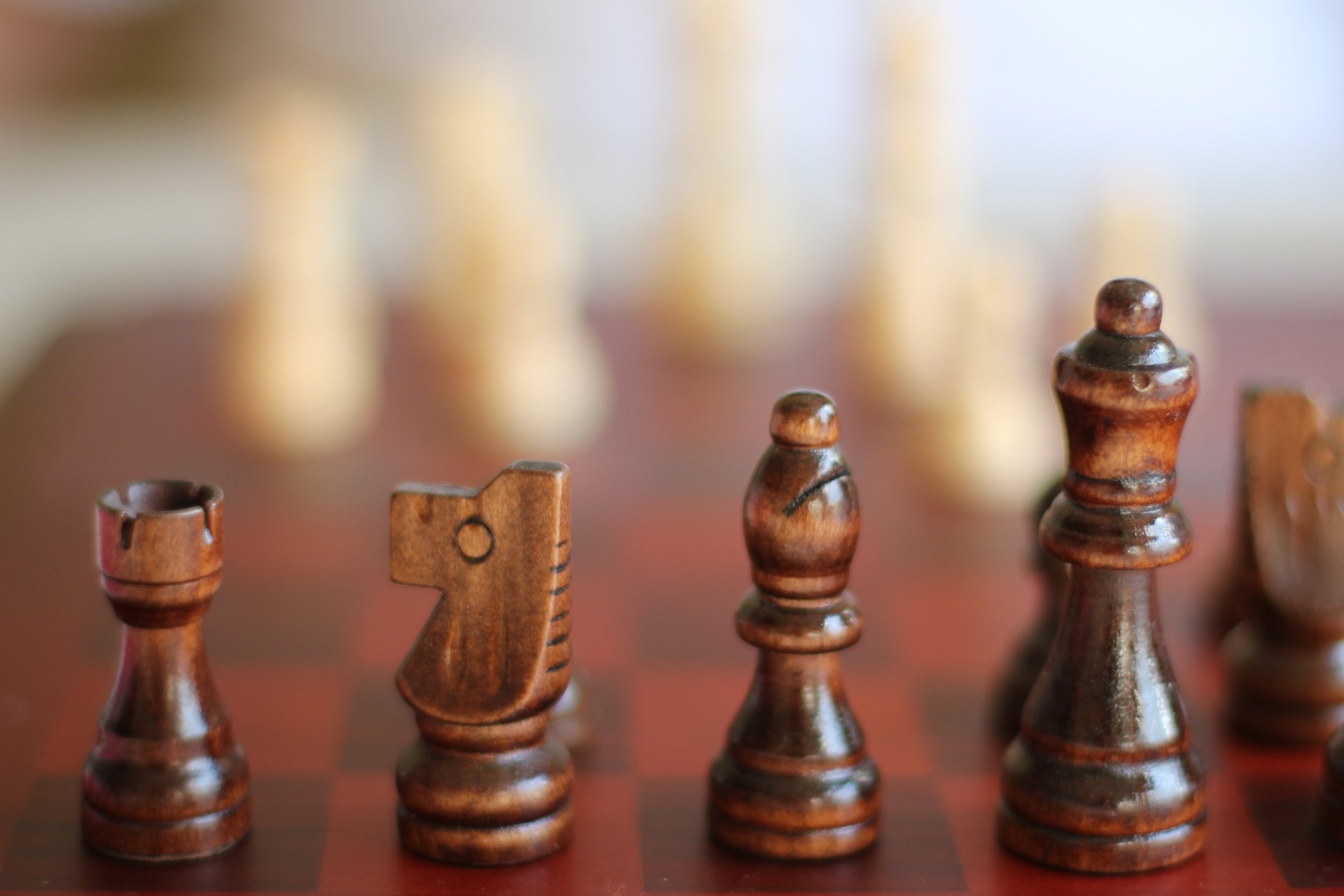 4K Ultra HD PC desktop wallpaper of a man-made carved wooden chess set: close-up of polished chess pieces on a board with shallow depth of field and warm bokeh background.