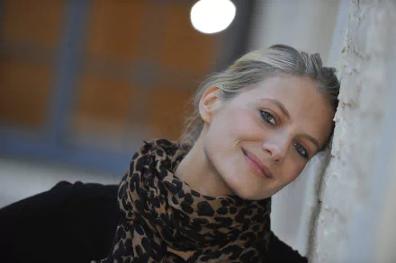 Portrait of French actress and celebrity Melanie Laurent smiling softly against a textured wall, captured in high-resolution 4K Ultra HD.