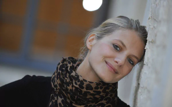 Portrait of French actress and celebrity Melanie Laurent smiling softly against a textured wall, captured in high-resolution 4K Ultra HD.