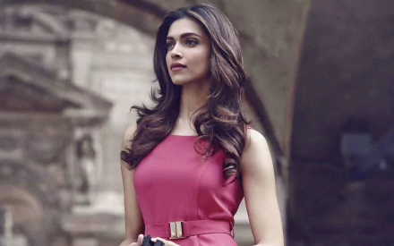 HD desktop wallpaper featuring celebrity Deepika Padukone, standing gracefully in a sleeveless pink dress, with an architectural background.