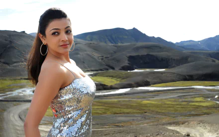 A stunning HD desktop wallpaper featuring celebrity Kajal Aggarwal in a shimmering outfit, set against a dramatic landscape of mountains and valleys.