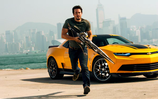 Mark Wahlberg runs with a weapon beside a yellow sports car in a scene from Transformers: Age of Extinction, set against a hazy city skyline. HD desktop wallpaper.