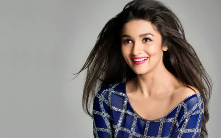 HD desktop wallpaper featuring celebrity Alia Bhatt with a bright smile, wearing a blue and silver checkered dress against a plain background.