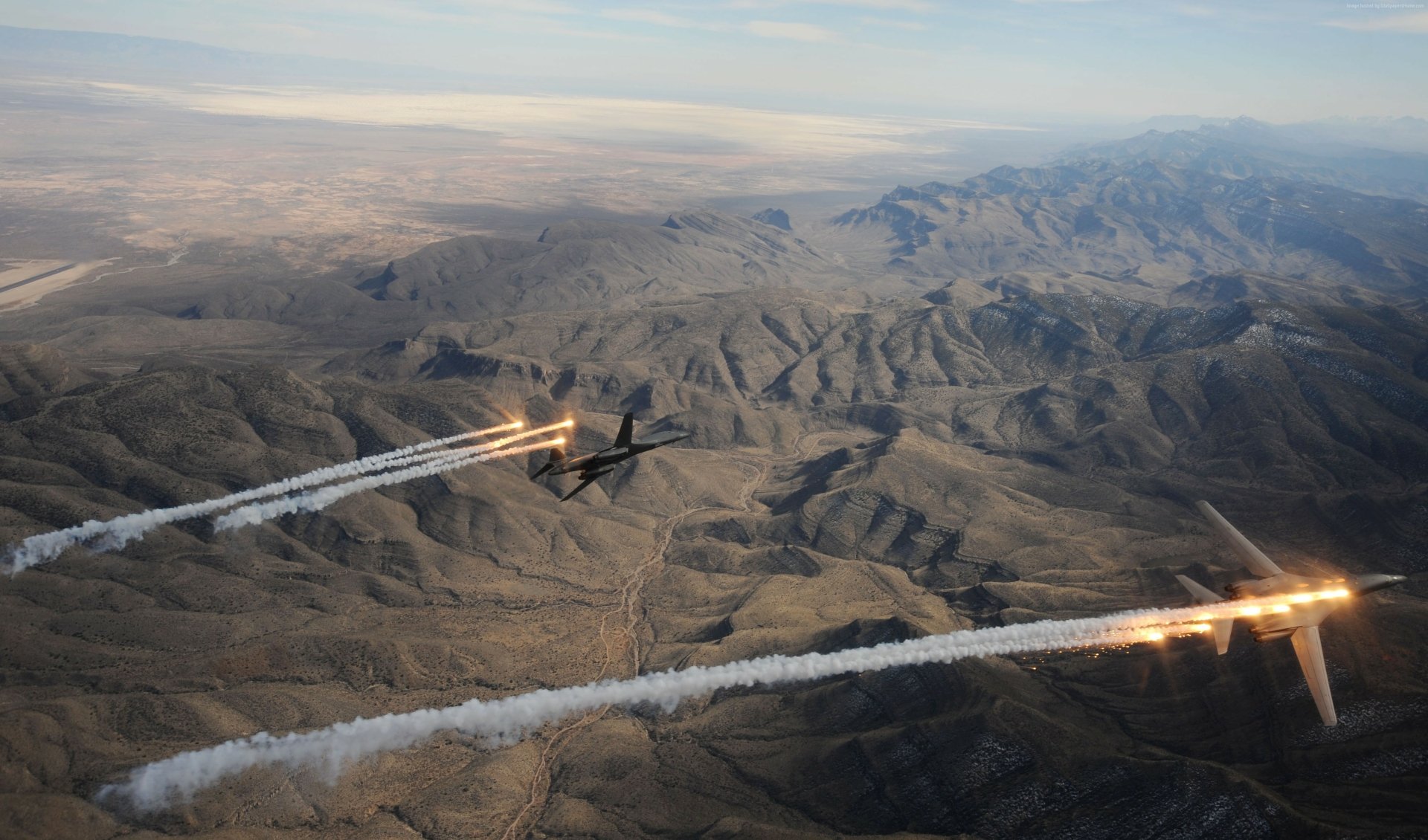 A 4K Ultra HD image of two Rockwell B-1 Lancer military bombers releasing flares over a rugged desert landscape.
