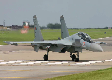 A high-definition desktop wallpaper featuring a Sukhoi Su-30 military jet on a runway, set against a backdrop of a grassy airfield and clear sky.