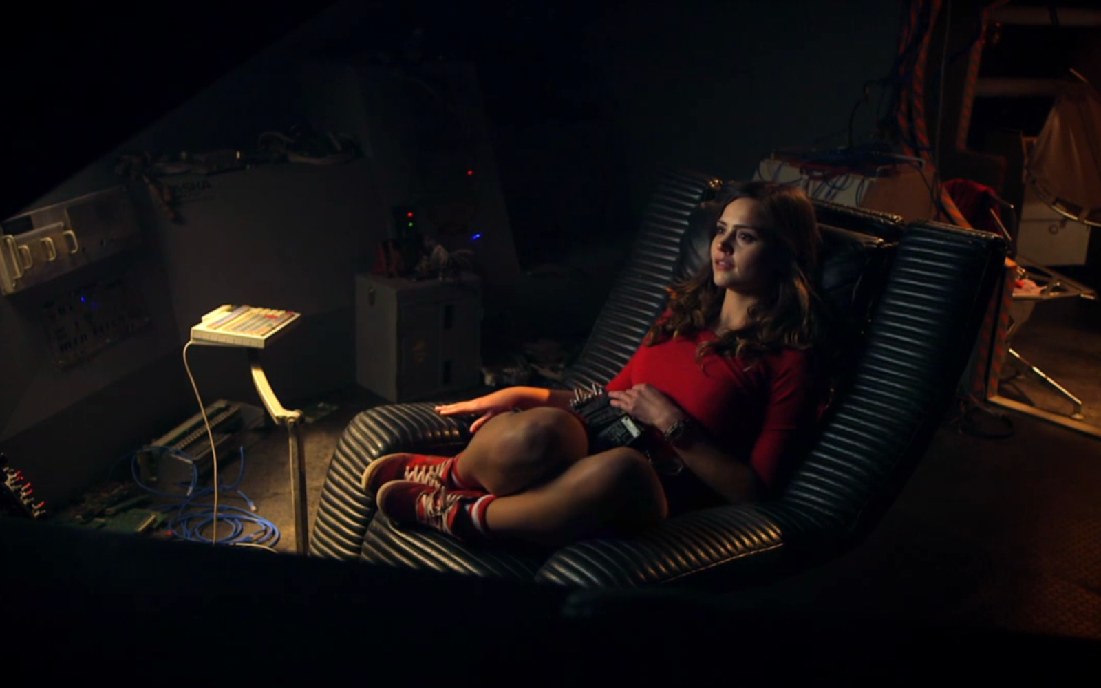 Clara Oswald, portrayed by Jenna Coleman, relaxes in a futuristic chair amidst a dimly lit setting in this HD Doctor Who wallpaper, capturing her intriguing character from the series.