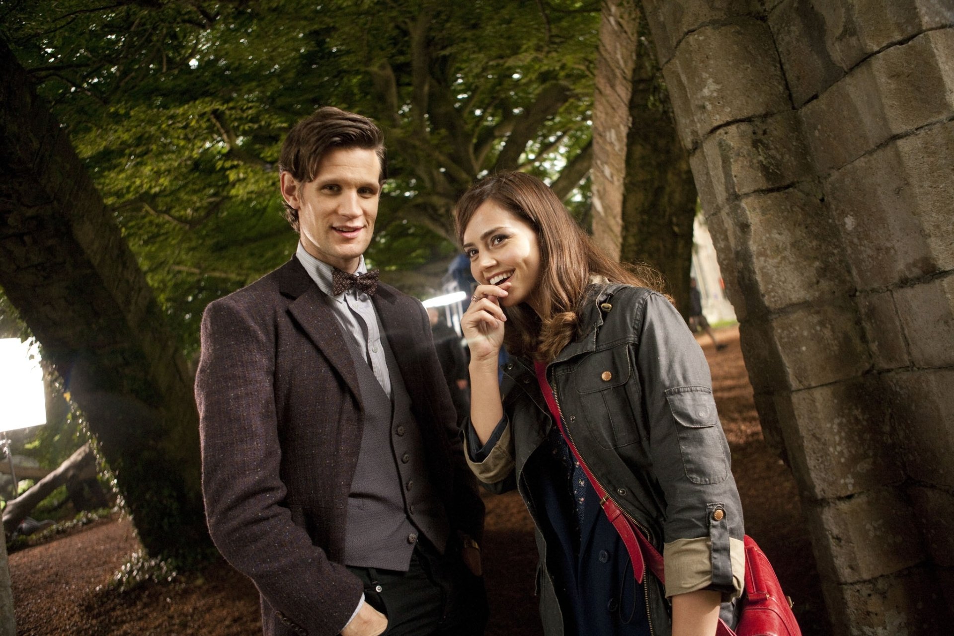 HD desktop wallpaper featuring Matt Smith and Jenna Coleman from the TV show Doctor Who (2005), standing outdoors with a background of stone arches and trees.