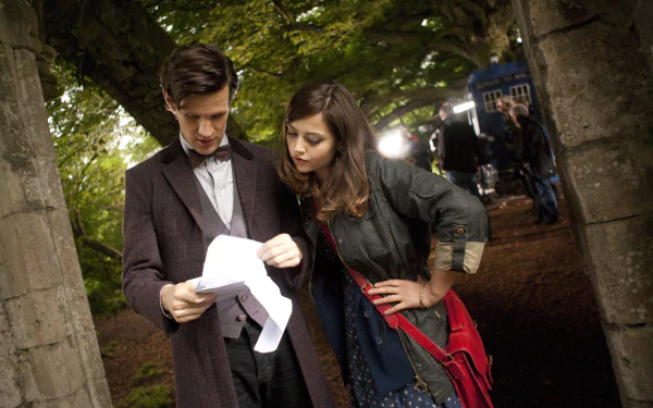 Matt Smith and Jenna Coleman as characters from Doctor Who (2005) on set outdoors, shown reviewing a script in a 4K Ultra HD PC desktop wallpaper and background.
