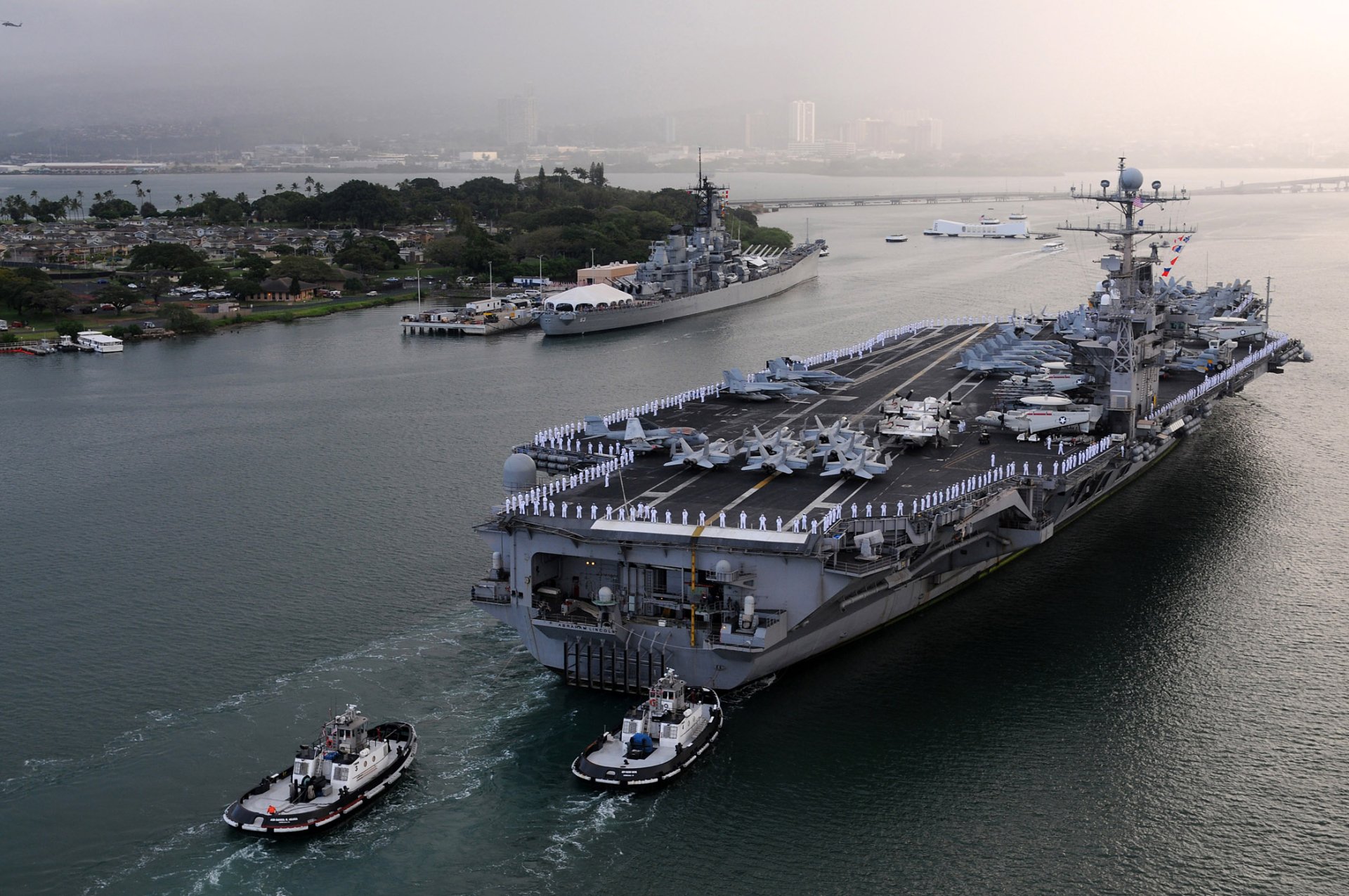 HD PC desktop wallpaper: US Navy aircraft carrier USS Abraham Lincoln (CVN-72) warship escorted by tugs through a harbor, military flight deck with parked aircraft.