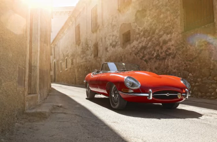 A vibrant red Jaguar E-Type convertible parked on a sunlit cobblestone street, captured in stunning detail for a 4K Ultra HD PC desktop wallpaper.