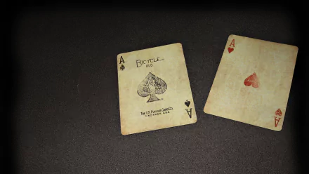 A high-definition desktop wallpaper featuring two playing cards—an Ace of Spades and an Ace of Hearts—laid against a dark, textured background.