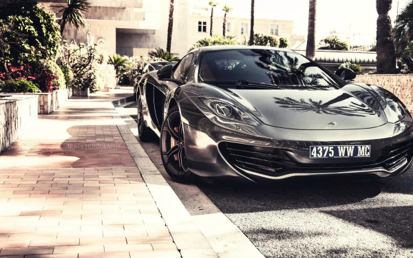 A sleek McLaren MP4-12C parked on a sunlit pathway, surrounded by lush greenery, showcased as a stunning HD desktop wallpaper and background.