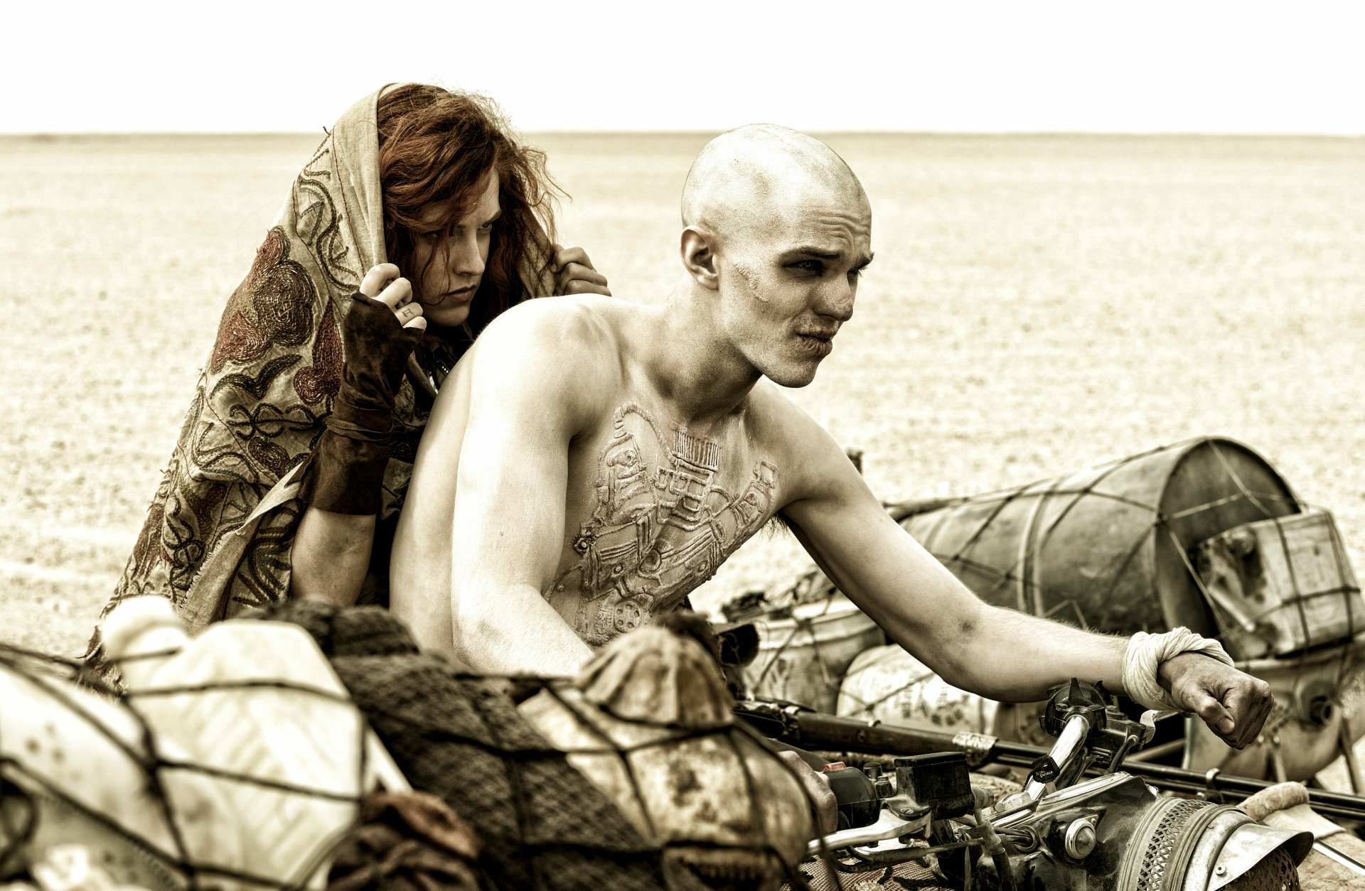 4K Ultra HD wallpaper featuring Capable (Riley Keough) and Nux (Nicholas Hoult) from Mad Max: Fury Road in a desert scene on a rugged vehicle.