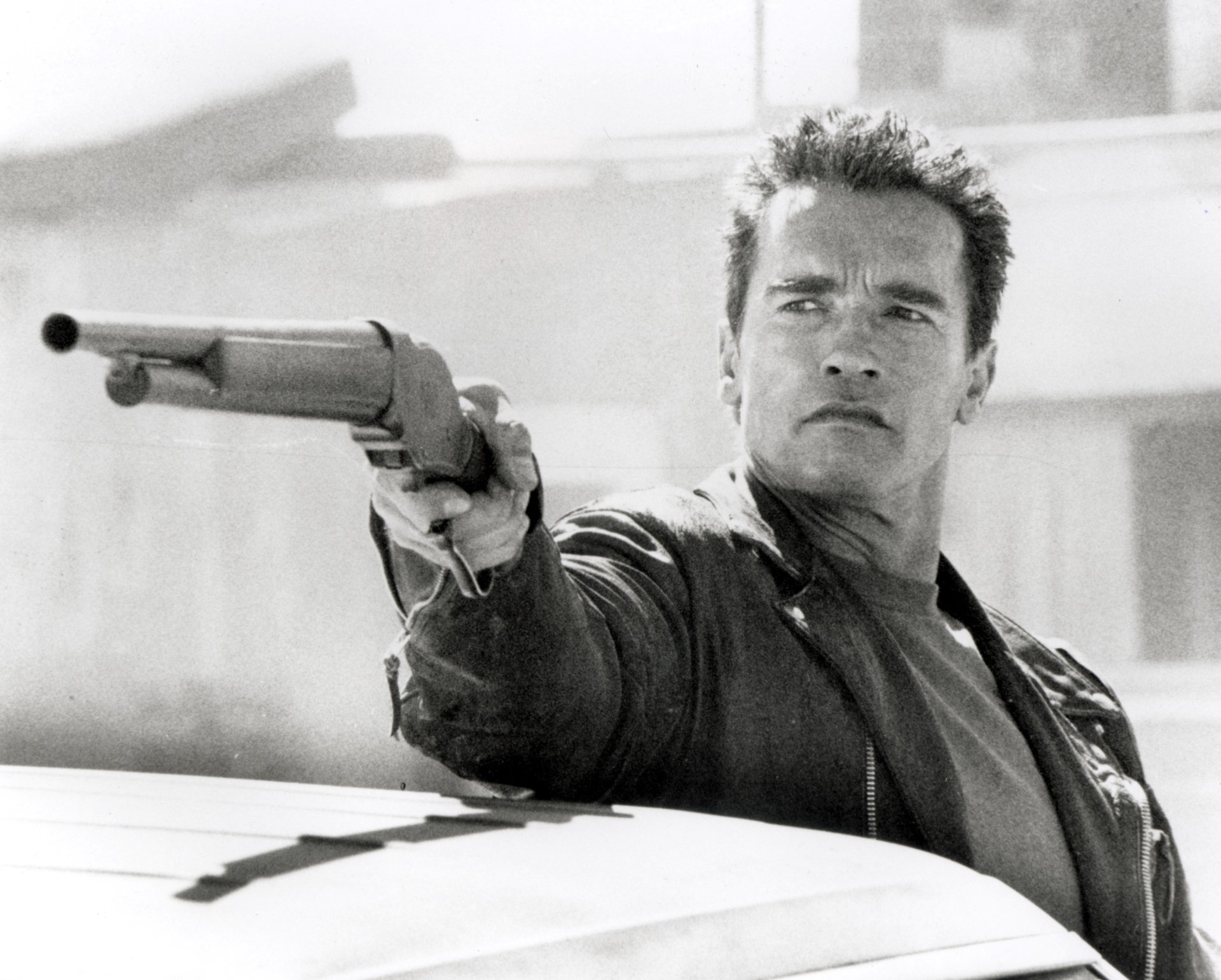 Arnold Schwarzenegger as the Terminator aiming a shotgun, capturing an intense moment from Terminator 2: Judgment Day in this striking black-and-white HD wallpaper.
