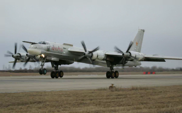 A Tupolev Tu-95 military bomber landing on a runway, showcasing its distinctive propeller design against a cloudy backdrop. A striking HD desktop wallpaper option.