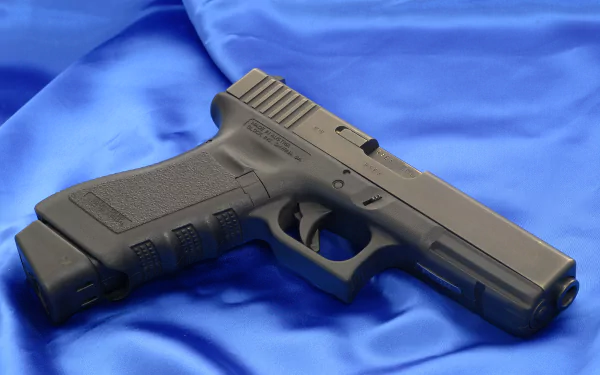 HD desktop wallpaper of a Glock pistol placed on a vibrant blue fabric background. The image highlights the firearm's sleek design and detailed craftsmanship.