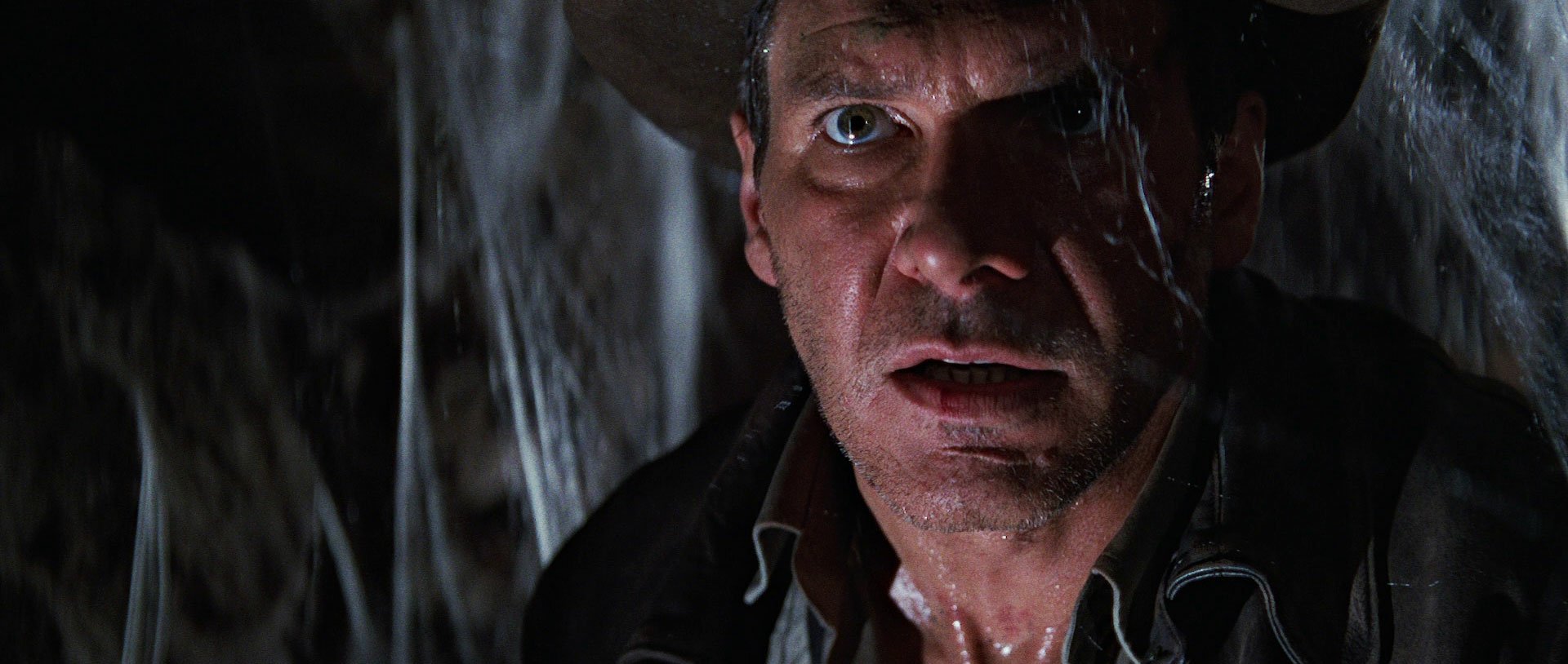 Close-up of Harrison Ford as Indiana Jones in a dark, rainy scene from the movie Indiana Jones and the Temple of Doom, presented as an HD PC desktop wallpaper.