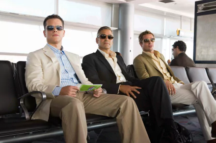 Three suave men in suits and sunglasses sit in an airport terminal — Ocean's Thirteen movie-style 4K Ultra HD PC desktop wallpaper.
