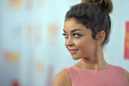HD PC desktop wallpaper featuring celebrity Sarah Hyland smiling and looking to the side with her hair styled in a high bun and wearing a pink sleeveless top.