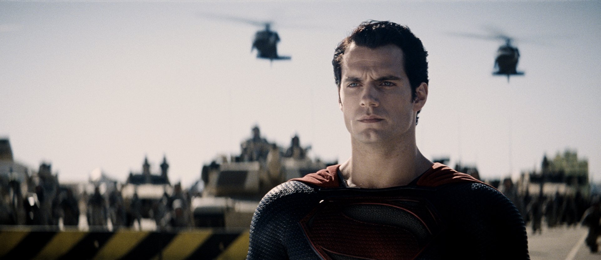 Superman, portrayed by Henry Cavill, stands resolutely amid helicopters, captured from the film Man of Steel, set against a dramatic sky in this HD desktop wallpaper.