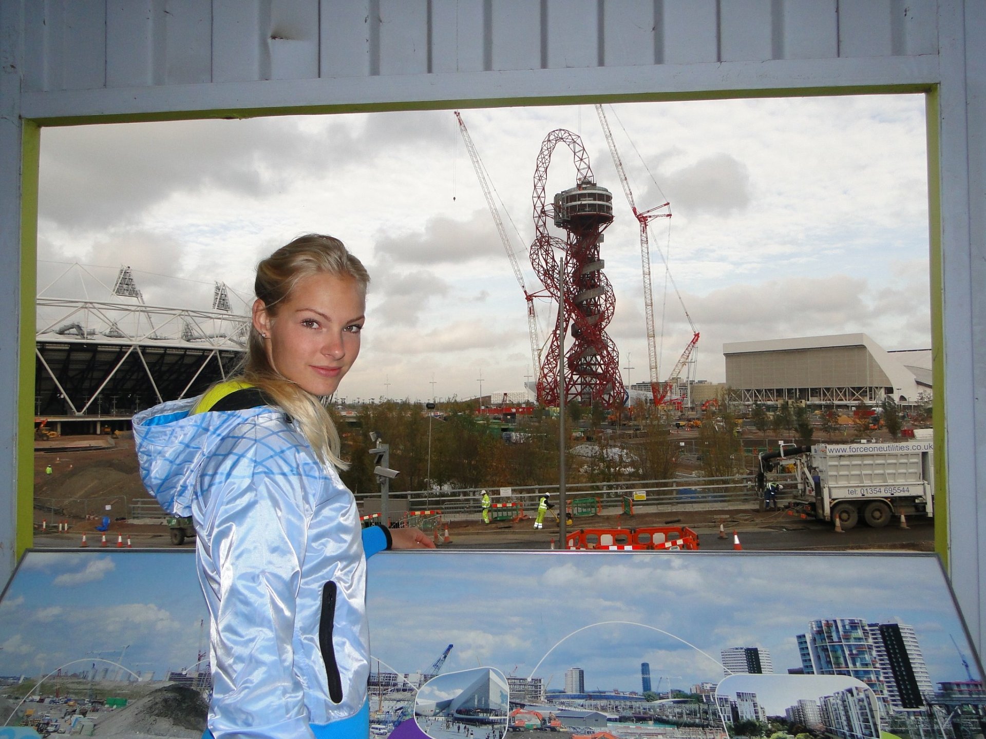 HD PC desktop wallpaper: a female athlete in a blue jacket smiles in front of a sports-themed cityscape featuring an Olympic stadium and observation tower.