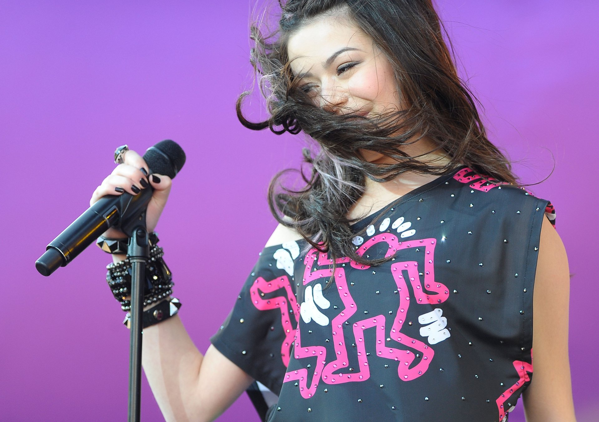 2K Quad HD PC desktop wallpaper and background: female celebrity singer holding a microphone, hair blowing, smiling against a vibrant purple backdrop.