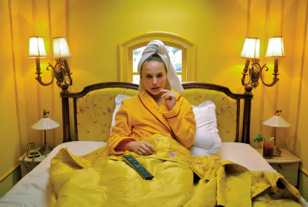 HD desktop wallpaper featuring Natalie Portman in a scene from the movie The Darjeeling Limited, sitting on a bed with a yellow backdrop and cozy lighting.