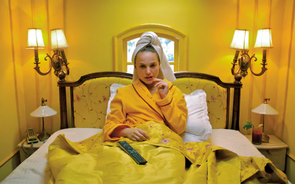 HD desktop wallpaper featuring Natalie Portman in a scene from the movie The Darjeeling Limited, sitting on a bed with a yellow backdrop and cozy lighting.