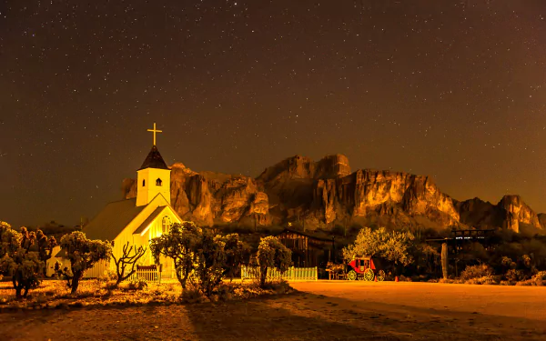 A serene nighttime view of a church illuminated under a starry sky with rocky cliffs in the background, captured in stunning 4K Ultra HD for PC desktop.