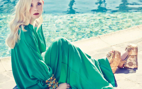 HD desktop wallpaper featuring celebrity Elle Fanning in a flowing green dress, seated by a pool with sparkling blue water in the background.