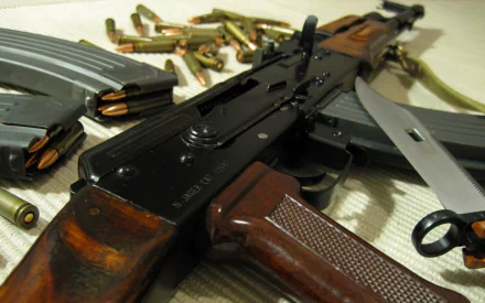 A close-up view of an AK-47 rifle with ammunition and magazines scattered around, featuring rich textures and details, set against a neutral background for a striking HD desktop wallpaper.