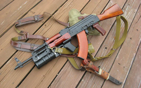 An AK-47 rifle rests on a wooden surface, surrounded by straps and a green canvas bag, creating a striking desktop wallpaper and background.