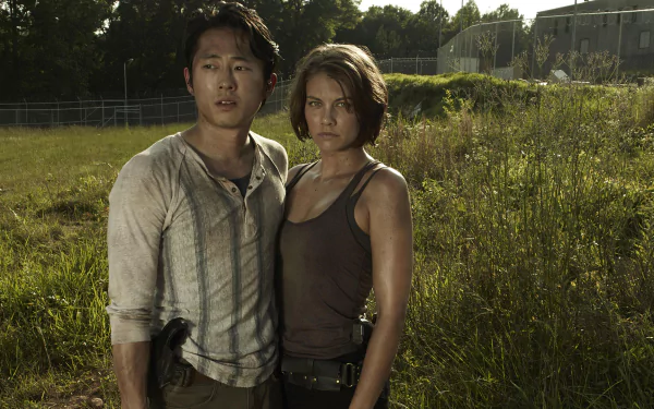 Glenn Rhee and Maggie Greene, portrayed by Steven Yeun and Lauren Cohan, stand together in a tense moment from the TV show The Walking Dead. HD desktop wallpaper featuring their close bond.