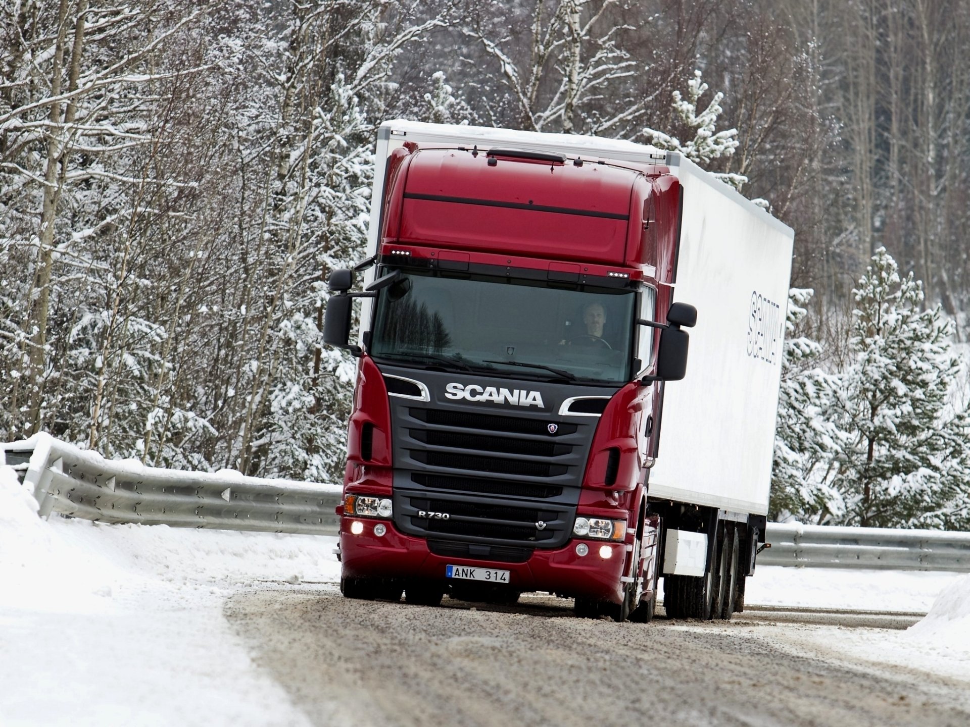 HD desktop wallpaper featuring a red Scania truck driving on a snowy road surrounded by snow-covered trees.