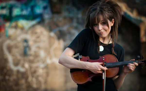 HD PC desktop wallpaper of Lindsey Stirling playing the violin, set against a blurred graffiti-covered wall, capturing a music-themed artistic vibe.