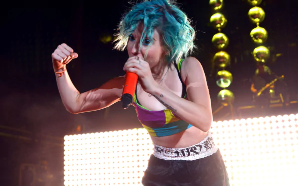 Energetic female rock singer with teal hair holding an orange mic amid stage lights — music; 2K Quad HD PC desktop wallpaper background.